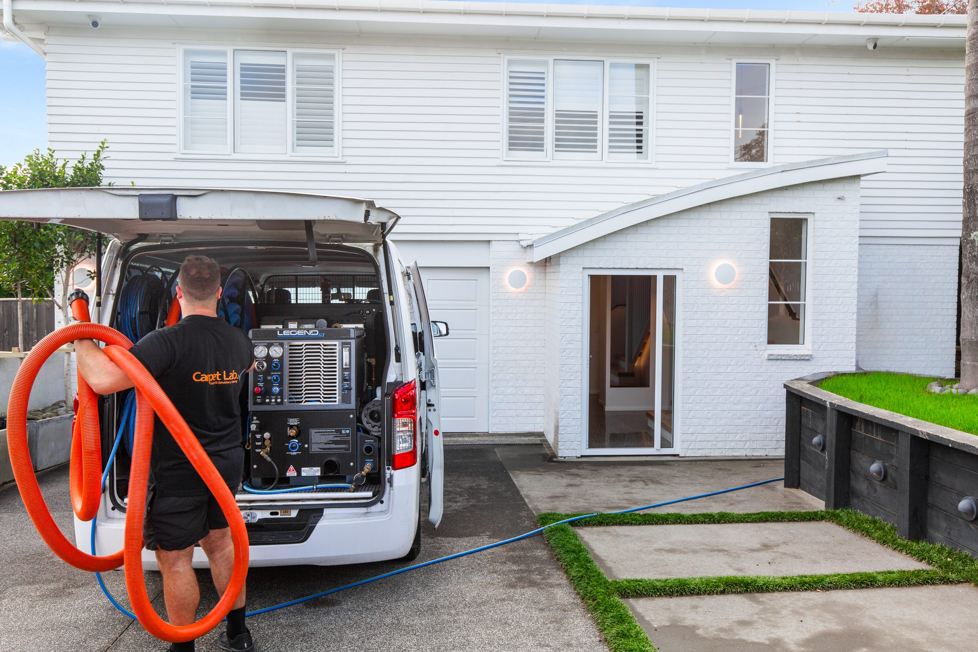 Carpet Lab technician unloading orange cleaning hoses beside the service van at an Auckland home